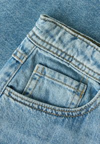 Zbliżenie na jasnoniebieskie dżinsy z denimu, pokazujące przednią kieszeń z mniejszą kieszonką na monety oraz widoczne detale przeszyć.