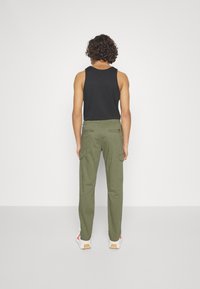 Black tank top, olive green cargo pants with multiple pockets and zippers, worn with white and red sneakers, viewed from the back.