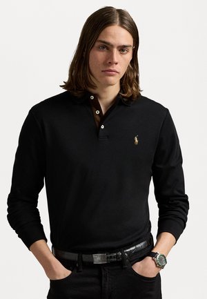 Polo a maniche lunghe nera con colletto a contrasto marrone, dotata di un piccolo logo ricamato. Indossata con jeans scuri e una cintura di pelle.