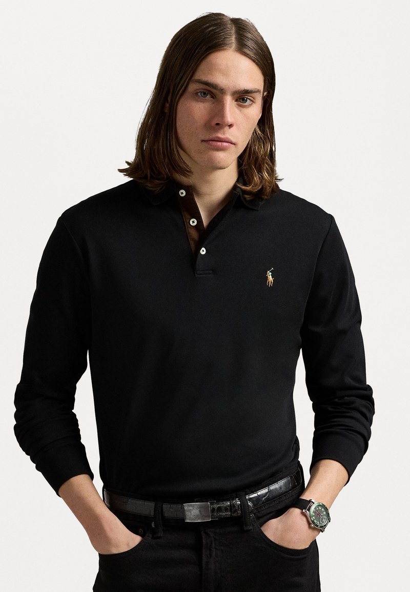 Black long-sleeve polo shirt with a brown contrast collar, featuring a small embroidered logo. Worn with dark jeans and a leather belt.