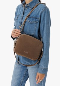 Brązowa zamszowa torebka na ramię z zamkiem błyskawicznym, prostokątnym kształcie i regulowanym paskiem. Logo marki widoczne z przodu.