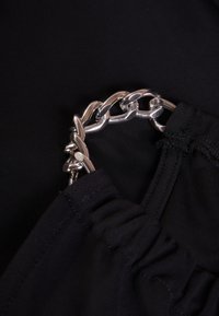 Tela negra con un detalle decorativo de cadena plateada, que presenta un diseño de borde fruncido y una textura suave.