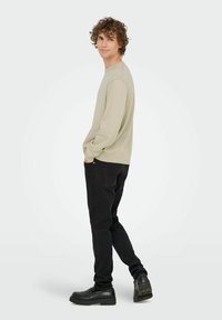 Beige longsleeve shirt gecombineerd met zwarte jeans en zwarte schoenen. Het shirt heeft een ronde halslijn en een ontspannen pasvorm, met ribgebreide manchetten.