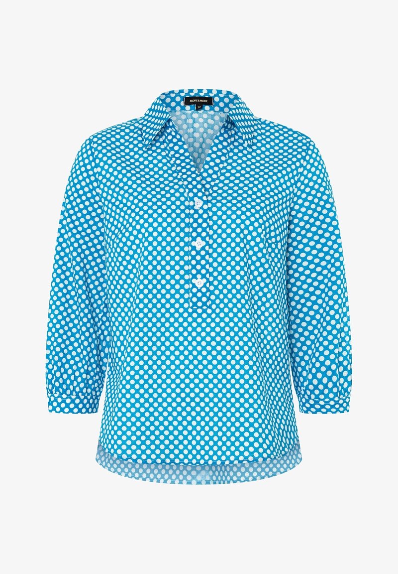 Blå skjorte med hvidte polka prikker, der har krave, trekvart ærmer og en forlommes. Lavet af letvægtsstof.