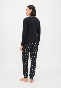 Top negru cu mâneci lungi asortat cu pantaloni de pijama negri cu buline albe. Material moale, croială lejeră și manșete elastice.