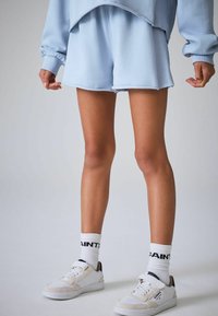 Šviesiai mėlynas džemperis ir atitinkami šortai iš minkštos medžiagos. Balti sportbačiai su juodu akcentu ir baltos prekės ženklo kojinės. Kasdienis stilius.