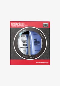 De verpakking van de Smashbox Test Shot Primer Duo heeft een rode rand met een zwarte textuur achtergrond. Twee tubes: een zilveren en een blauwe, duidelijk gelabeld.