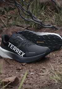 Scarpe da trail running Terrex nere e grigie su terreno roccioso con suole in gomma Continental e lacci e marchio visibili.