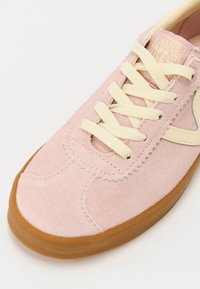Svijetlopinkane suede tenisice s kremastim vezicama, gumenim potplatom i malim smeškim logotipom. Detalji šivenja duž vrha.