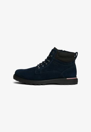 Stivaletto in suede blu navy con collo imbottito nero, chiusura a lacci, linguetta per estrazione e suola nera robusta con dettagli a strisce rosse e bianche.
