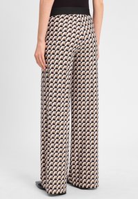 Brede pantalons met een zwart en beige golfpatroon. Heeft een zwarte elastische tailleband en een gladde, lichte stoftextuur.
