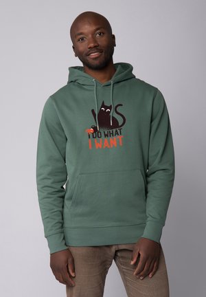 Groene hoodie van een katoenmengsel met een voorzak, voorzien van een afbeelding van een zwarte kat en de tekst "IK DOE WAT IK WIL" in het rood.