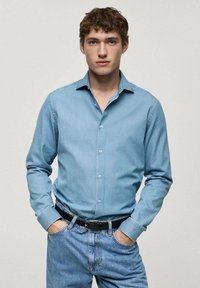 Lichtblauwe denim overhemd met een karakteristieke kraag, knoopsluiting en lange mouwen, gecombineerd met lichtblauwe jeans en een zwarte riem.