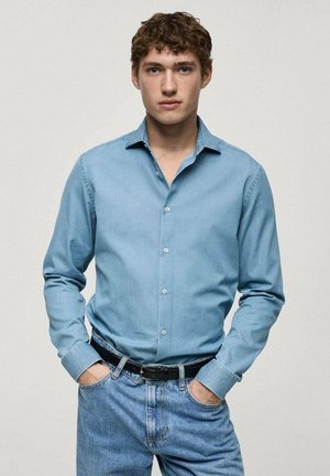 Camicia di jeans azzurri chiari con colletto a punta, chiusura a bottoni e maniche lunghe, abbinata a jeans azzurri chiari e una cintura nera.