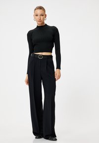 Cropped top nero a costine con maniche lunghe abbinato a pantaloni neri a vita alta e ampia gamba, con una cintura nera sottile dotata di una fibbia circolare.