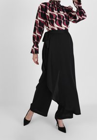 Långärmad blus med ett vågigt mönster i rosa, svart och kräm; matchad med svarta byxor i omslag med en asymmetrisk fåll.