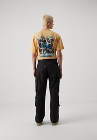 Gul grafisk t-skjorte med teksten "ROAD TRIP" og design, sammen med svarte cargo-bukser med sidelommer og en avslappet passform.