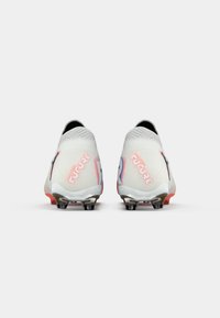 Een paar witte soccer-schoenen met "Future" branding in roze, gezien vanaf de hiel, met een weergave van de gestifte zolen op een effen achtergrond.