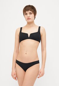Svart bikiniset som har en kort överdel med V-formad halsringning och breda axelband, ihop med lågbyxade bikiniunderdelar, med en mjuk textur.