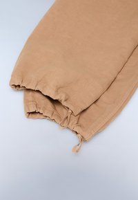Beige katoen broek met elastische boorden, voorzien van een aangetrokken koorddetail en zichtbare stiksels langs de zoom. Zacht, lichtgewicht materiaal.