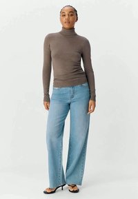 Brown turtleneck sweater paired with light blue wide-leg jeans, featuring a smooth texture and relaxed fit. Black heeled sandals complete the look.