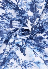 Blauw en witte stof met een gedetailleerd toilepatroon dat bomen en mensen in historische kleding toont, gevouwen met een centrale spiraal.
