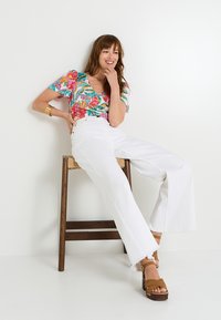 Top de manga corta con estampado floral y escote en V; jeans blancos de tiro alto y pierna ancha; sandalias de plataforma marrones; taburete de madera.