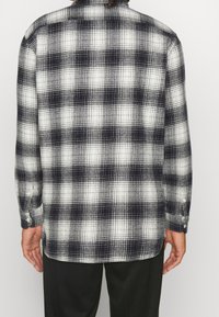 Chemise en flanelle à carreaux noir et blanc avec manches longues, poignets à boutons et col classique, dotée d'un tissu doux et texturé.