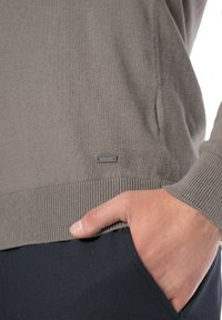 Szary sweter dzianinowy z ściągaczem, z małą metalową metką marki. Zbliżenie ukazuje miękką teksturę i rękę umieszczoną w kieszeni.