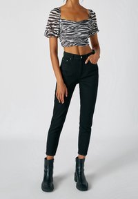 Černé vysoké džínsy doplněné o krátký top s černobílým pruhovaným vzorem zebry, který má nabírané rukávy a čtvercový výstřih. Černé kotníkové boty.