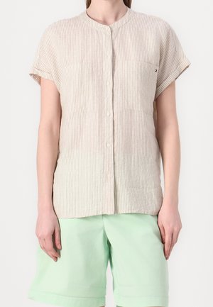 Beige short-sleeve button-up shirt with thin vertical stripes paired with light green knee-length shorts on a standing person.
