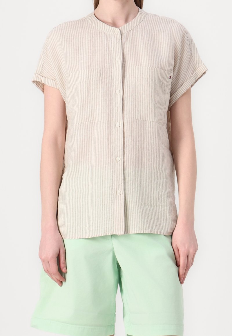 Chemise beige à manches courtes avec fines rayures verticales, associée à un short vert clair longueur genoux sur une personne debout.