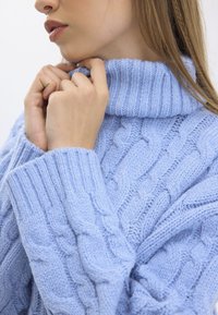 Light blue cable-knit turtleneck sweater featuring ribbed detailing at the collar and cuffs, with a soft, textured finish and relaxed fit.