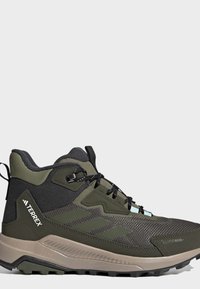 High-top olive green and black Terrex hiking shoe with textured sole, black laces, and Climawarm insulation label on toe area.