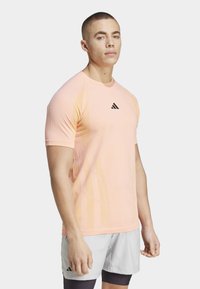 Camiseta deportiva de manga corta, de color rosa claro, hecha de tejido transpirable, con un logo negro de Adidas en el pecho y paneles laterales texturizados.