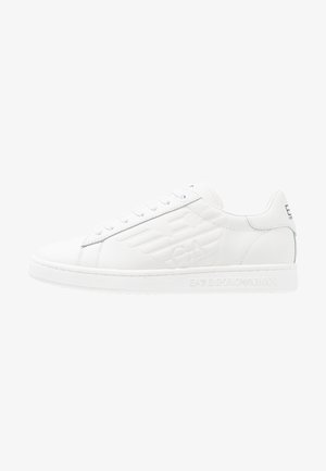 Baskets en cuir blanc à texture lisse, avec un design à lacets, un logo embossé sur le côté et une semelle en caoutchouc texturée. Style minimaliste.