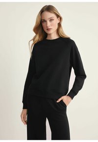 Czarna bluza z luźnym krojem, okrągłym dekoltem, prą żkowanymi mankietami i dołem. Wykonana z gładkiego materiału, z raglanowymi rękawami i minimalistycznym designem.