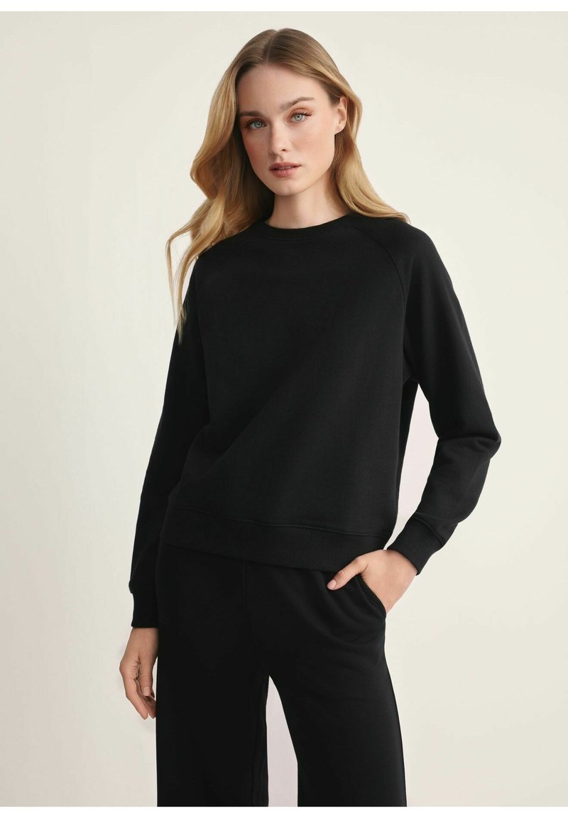Czarna bluza z luźnym krojem, okrągłym dekoltem, prążkowanymi mankietami i dołem. Wykonana z gładkiego materiału, z raglanowymi rękawami i minimalistycznym designem.