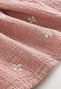 Pink muslin fabric featuring a textured surface with embroidered white floral patterns, displaying soft folds and a lightweight appearance.