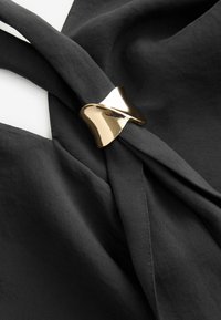 Zwart stof met een gladde textuur, voorzien van een gedraaide ontwerp dat wordt samengehouden door een gouden metalen accent.