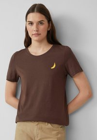 Bruine katoenen T-shirt met korte mouwen en een ronde halslijn, met op de borst een kleine gele bananagrafiek.