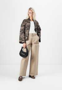 Zwart en beige zebra-print jasje, witte top, beige wijde broek, zwarte handtas en schoenen met luipaardprint. Neutrale kleuren en verschillende texturen.