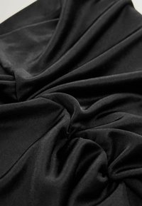 Must mustritekstiine kangas, millel on peen tekstuur, lahtiselt kogutud ja keeratud, luues pehmeid voldikuid ja heledaid kohti valguse taustal.