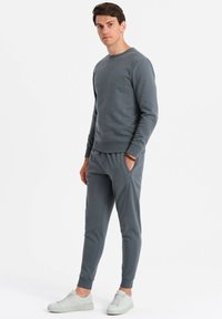 Grauer Fleece-Pullover und passende Jogginghose, mit einem Rundhalsausschnitt, gerippten Bündchen und Taschen. Kombiniert mit hellgrauen Sneakers.