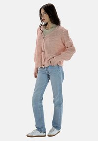 Ljust rosa, ribbad cardigan med långa ärmar och knappstängning. Bärs över en neutral topp, ihop med ljusblå jeans och vita sneakers.