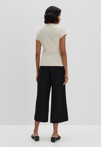 Cream ribbed short-sleeve top paired with loose black culottes, featuring a straight cut and flat black slide sandals. Minimalist design.