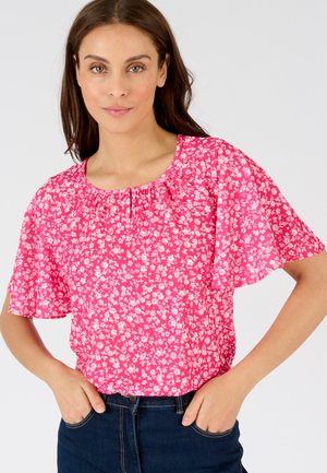 Blusa corta a maniche corte di colore rosa con scollo arricciato, caratterizzata da un motivo di piccoli fiori bianchi su uno sfondo vivace.