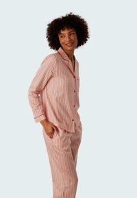 Röd och rosa randig pyjamas-set gjort av mjukt tyg. Långärmad topp med krage och ficka, matchande avslappnade byxor med sidofickor.