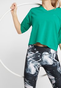 Zielona, krótkiego kroju, koszulka typu v-neck z krótkimi rękawami, połączona z czarnymi legginsami z białym, abstrakcyjnym wzorem i graficznymi detalami.