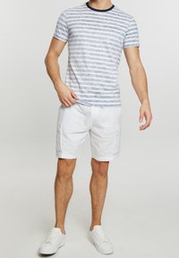Camiseta ligera a rayas en azul y blanco, combinada con shorts de carga blancos. Un cuello redondo ordenado y zapatillas blancas con cordones completan el conjunto.